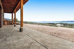 A covered outdoor area with a concrete floor, wooden pillars, and a view of a lake and distant buildings. - Mountain View Escape (Garden City)