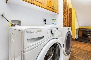 A front-loading Whirlpool Duet washer and dryer in a laundry room with wooden cabinets above and a black metal cage to the right. - Mountain View Escape (Garden City)