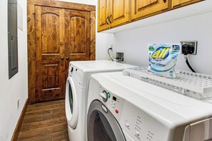 A laundry area with a washing machine and dryer, a wooden door, and a bag of laundry detergent. - Mountain View Escape (Garden City)