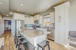 A modern kitchen with white cabinets, a granite countertop island, and bar stools. - Lakefront Retreat - Hot Tub, Game Room & Fire Pit (Garden City)