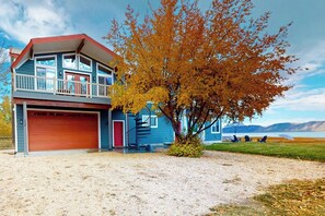 Une maison à deux étages avec une porte de garage rouge, un balcon et un arbre aux feuilles d’automne.