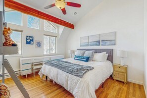 Ein Schlafzimmer mit einem Bett, einem Schreibtisch, einem Stuhl, einem Nachttisch, einer Lampe und einem Deckenventilator.