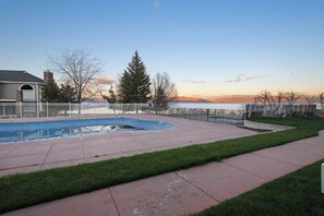 A backyard with a swimming pool, a fenced area, and a view of a body of water during sunset. - Bear Lake  View - Pool, Hot Tub & Game Room (Garden City)