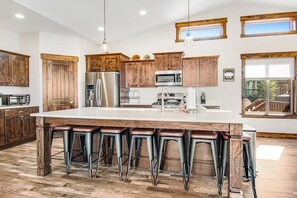 A spacious kitchen with a large island, wooden cabinets, stainless steel appliances, and bar stools. - Blue Bell - Lake Views, Pool, Hot Tub, Dogs OK (Garden City)