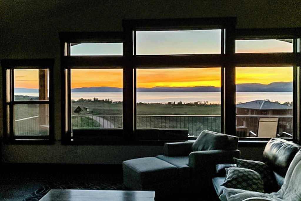 A room with a large window overlooking a landscape, a sofa, and a coffee table.