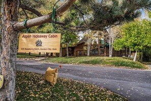 Een houten bordje voor Aspen Hideaway Cabin, met een lodge op de achtergrond.