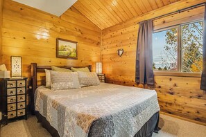 Een houten slaapkamer met een bed, nachtkastje, dressoir en een raam met gordijnen.