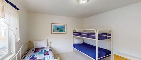 A room with a bunk bed, a single bed, a window with curtains, a framed picture on the wall, and a ceiling light fixture.