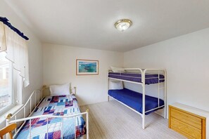 Ett rum med en våningssäng, en enkelsäng, ett fönster med gardiner, en inramad tavla på väggen och en taklampa.