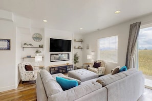 A living room with a large grey sofa, a flat-screen TV, and a window with blinds. - Garden City Glee - Mountain Views, Dogs Welcome (Garden City)