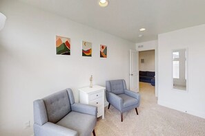 Quarto com duas poltronas cinzentas, uma mesinha de apoio branca e três quadros abstratos na parede.