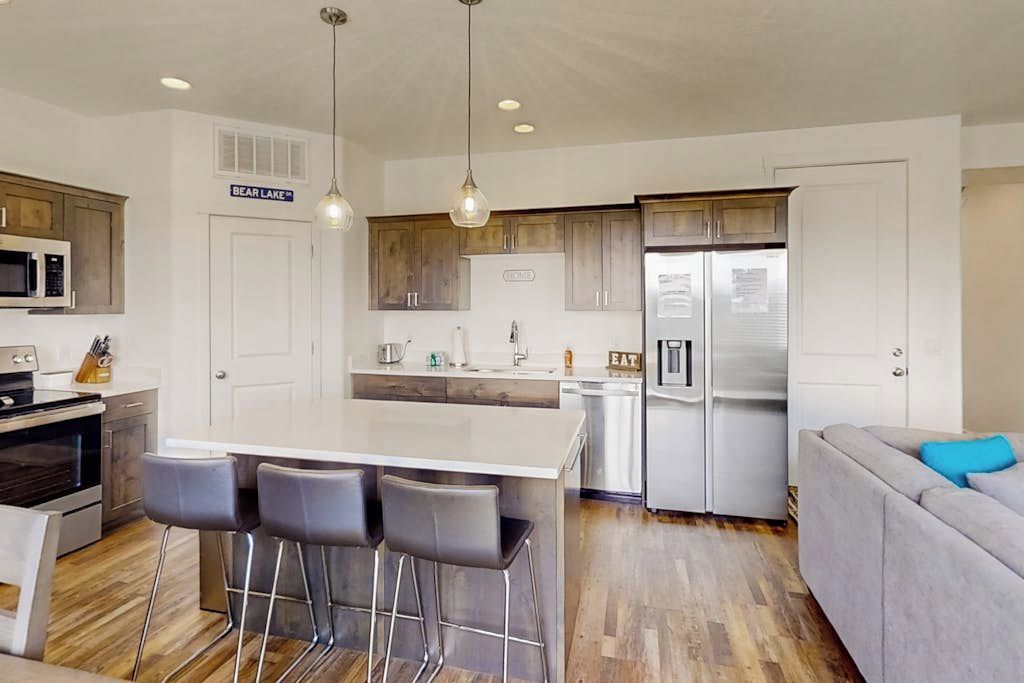A modern kitchen with a central island, bar stools, a refrigerator, and a microwave.