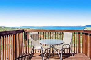 A wooden deck with a round table and four chairs, overlooking a body of water and distant hills. - Hilltop Hideaway - Lake Views, Hot Tub, Game Room (Garden City)