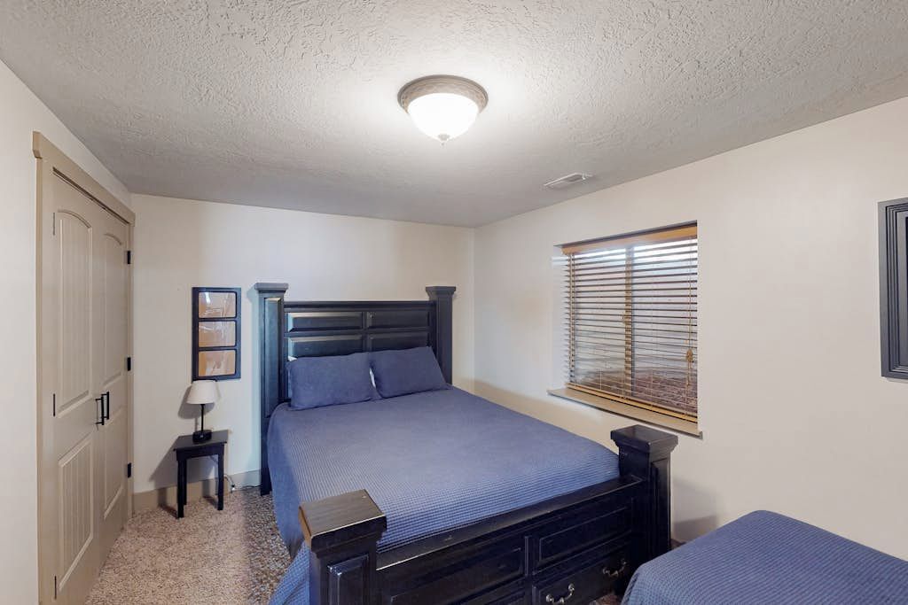 Une chambre à coucher avec un lit, des tables de chevet, une fenêtre avec des stores et une porte.