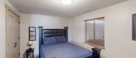 Ein Schlafzimmer mit einem Bett, Nachttischen, einem Fenster mit Jalousien und einer Tür.