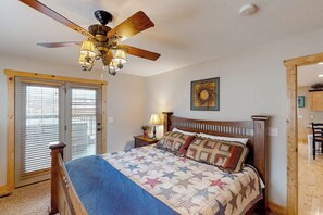 A bedroom with a bed, a ceiling fan, a nightstand with a lamp, and a door leading to another room. - Hilltop Hideaway - Lake Views, Hot Tub, Game Room (Garden City)