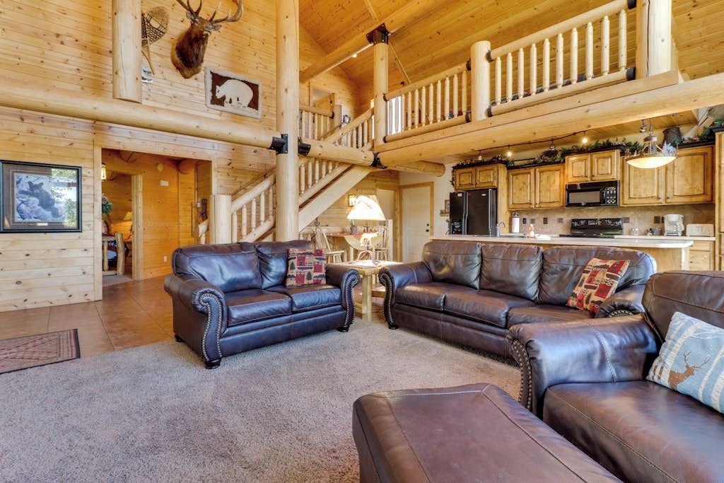 A spacious living area with leather sofas, a staircase, and a kitchen in a log cabin.
