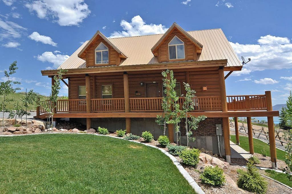 A two-story log cabin with a balcony, surrounded by a landscaped garden.