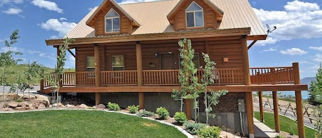 A two-story log cabin with a balcony, surrounded by a landscaped garden.