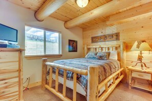 Un dormitorio tipo cabaña de madera con cama, televisor y ventana.