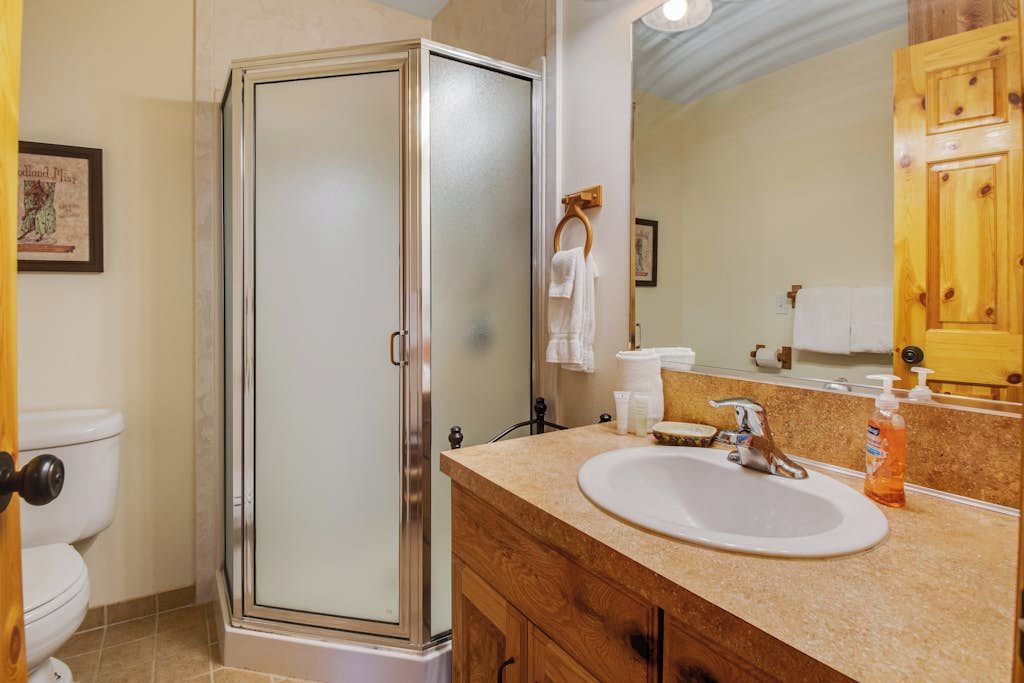 Een badkamer met een douche met glazen wand, een witte wastafel en houten kastjes.