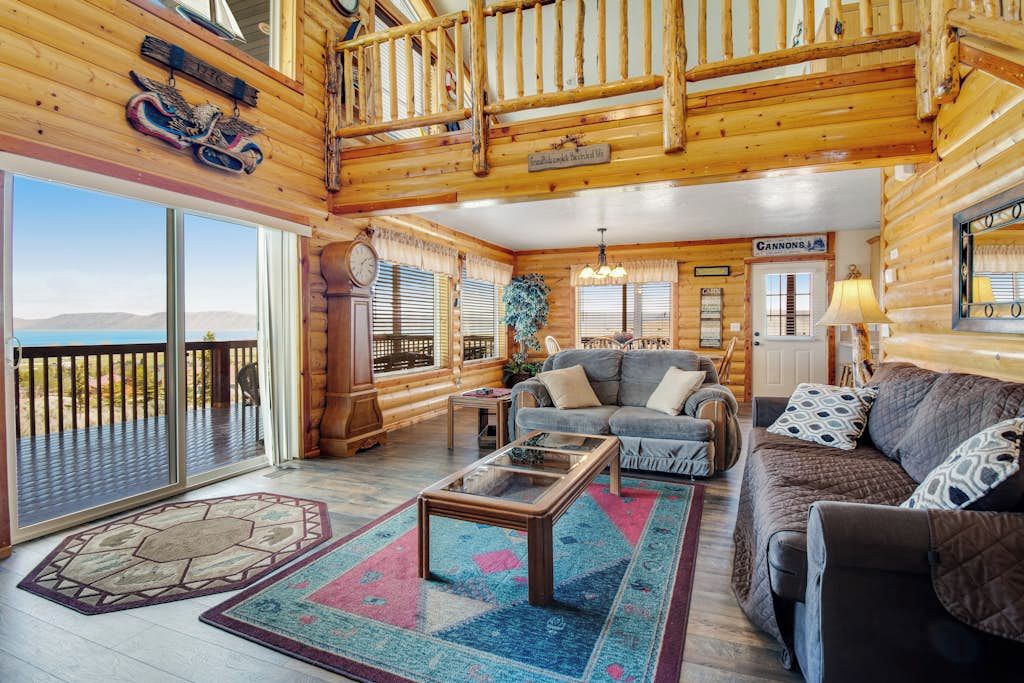 L’intérieur d’une cabane en rondins, avec une grande porte-fenêtre coulissante, un canapé, une table basse et une enseigne sur laquelle on peut lire « CANNONS ».