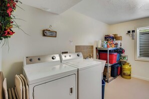 A laundry area with a front-loading washer and dryer, a shelf with storage bins, and a yellow gas canister. - Garden City Gem - Lake Views, Wraparound Deck (Garden City)