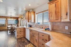 A kitchen with wooden cabinets, a sink, and a dining area with chairs. - Garden City Gem - Lake Views, Wraparound Deck (Garden City)