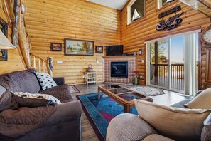 L’intérieur d’une cabane en rondins, avec une cheminée, un téléviseur et un balcon offrant une vue panoramique.