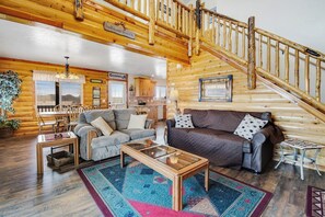 A log cabin interior with a staircase, a dining area, and a living room furnished with sofas and a coffee table. - Garden City Gem - Lake Views, Wraparound Deck (Garden City)