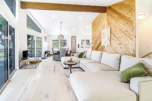 A modern living room with a large white sofa, a dining area, and a wooden accent wall.