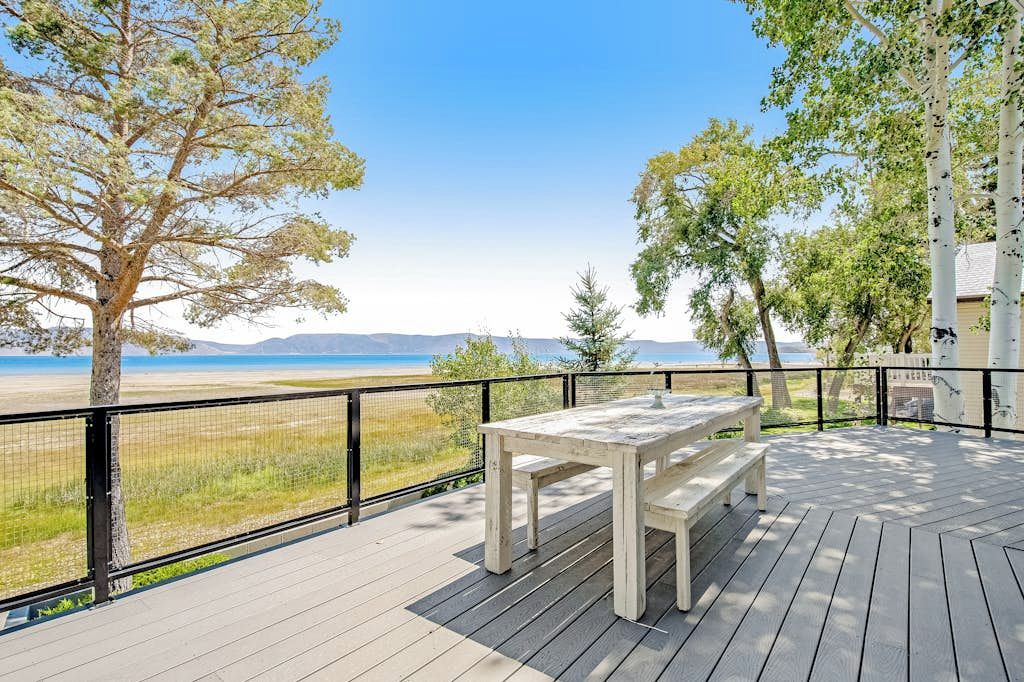 Eine Holzterrasse mit Tisch und Bänken mit Blick auf einen Strand.