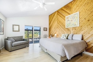 A bedroom with a bed, a sofa, a ceiling fan, and a wooden wall.