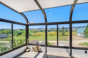 A room with large windows offering a view of a rural landscape, including fields and distant hills.