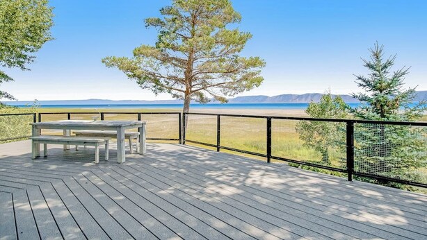 En träveranda med ett bord och bänkar med utsikt över en strand och berg.