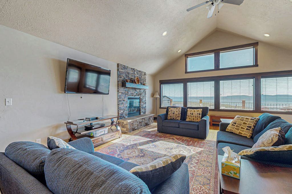 A living room with a stone fireplace, a flat-screen TV, and large windows.