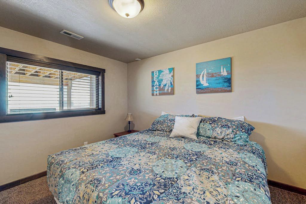 A bedroom with a large bed, a window with blinds, and two wall art pieces.
