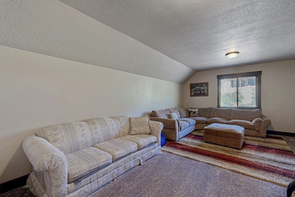 A living room with a large sectional sofa, a smaller sofa, and an ottoman. There is a window with blinds and a painting on the wall.