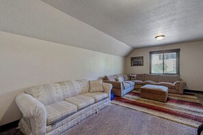 A living room with a large sectional sofa, a smaller sofa, and an ottoman. There is a window with blinds and a painting on the wall.