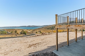 Un molo di legno con ringhiera in metallo che si affaccia su un paesaggio arido, colline lontane e un tratto d'acqua.