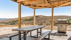 Ett takförsett utomhusområde med ett picknickbord och en grill.