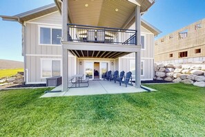 A two-story house with a balcony, outdoor seating area, and a stone wall. - Sweetwater Lakeview House (Garden City)