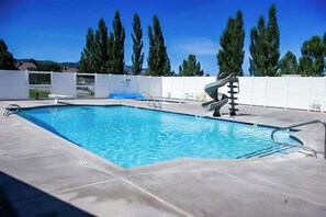 A swimming pool with a diving board, surrounded by a white fence and trees. - Sweetwater Lakeview House (Garden City)