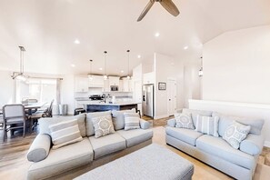 A modern living room with a sofa set, a dining area, and a kitchen in the background. - Sweetwater Lakeview House (Garden City)