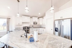 A modern kitchen with white cabinets, stainless steel appliances, and pendant lighting. - Sweetwater Lakeview House (Garden City)