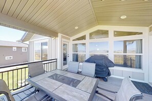 A covered patio with a table and chairs, large windows, and a view of the surrounding area. - Sweetwater Lakeview House (Garden City)