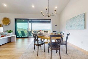 A dining area with a round table, chairs, a chandelier, a view through glass doors, and a painting on the wall. - Hillside Retreat - Private Pickleball, Near Lake (Garden City)