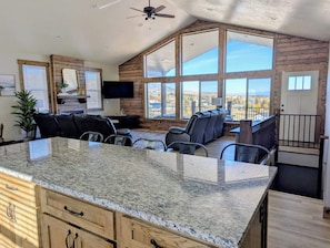 A spacious living area with a large kitchen island, a fireplace, and a balcony with a view. - The Bear Lake Spot - Lake Views & Wet Bar (Garden City)