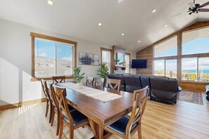 A spacious dining area with a wooden table and chairs, a sofa, and large windows offering a view. - The Bear Lake Spot - Lake Views & Wet Bar (Garden City)