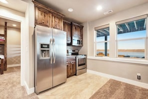 A kitchen with stainless steel appliances, wooden cabinets, and a view through large windows. - Two Bear Lodge - Sleeps 40, Pools & Beach Access (Fish Haven)